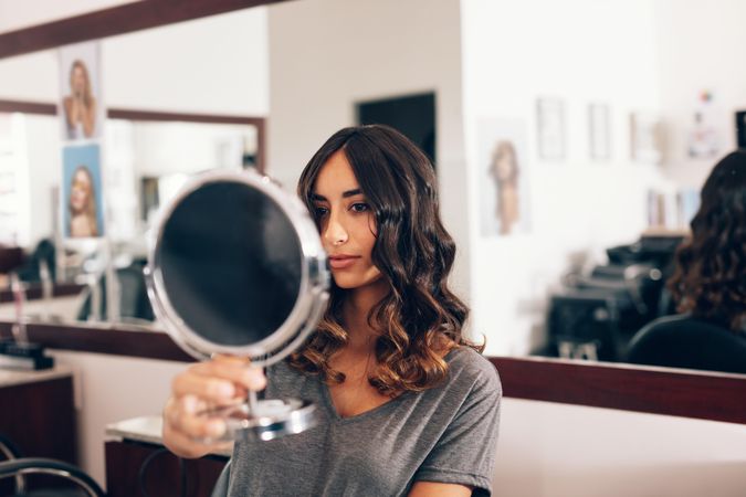 Young woman holding small round mirror to view styled hair