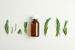 Flat lay composition with rosemary oil and leaves on plain background, space for text