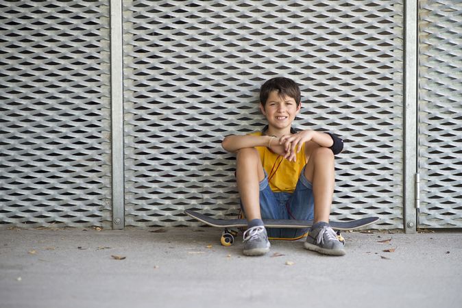 Smiling teen skateboarder sitting down for outdoors portrait