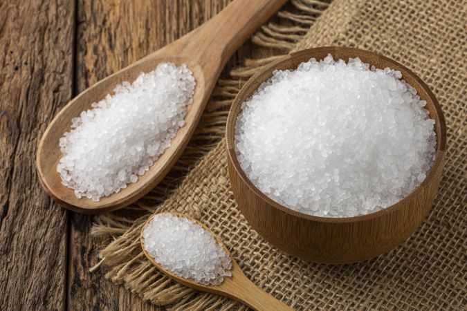 Coarse salt in bowl on wooden background.
