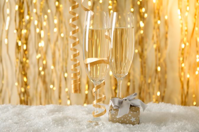 Champagne glasses and gift against background with golden ribbons, space for text