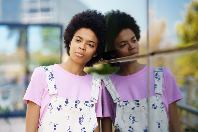 Female in floral overalls leaning head on window outside