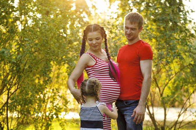 Pregnant woman reaching ahead for her child with partner in a sunny park