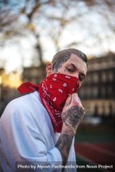 Young tough guy in red bandana with face tattoos furrowing brow at camera outside 5r96Z0