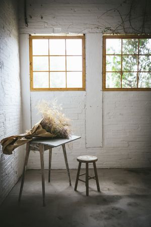 Bunch of plant in paper on table near stool in grey room