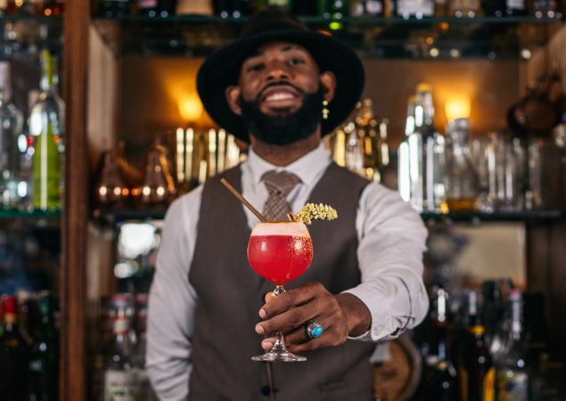 Stylish Black bartender pouring a cocktail and decorating it with garnish
