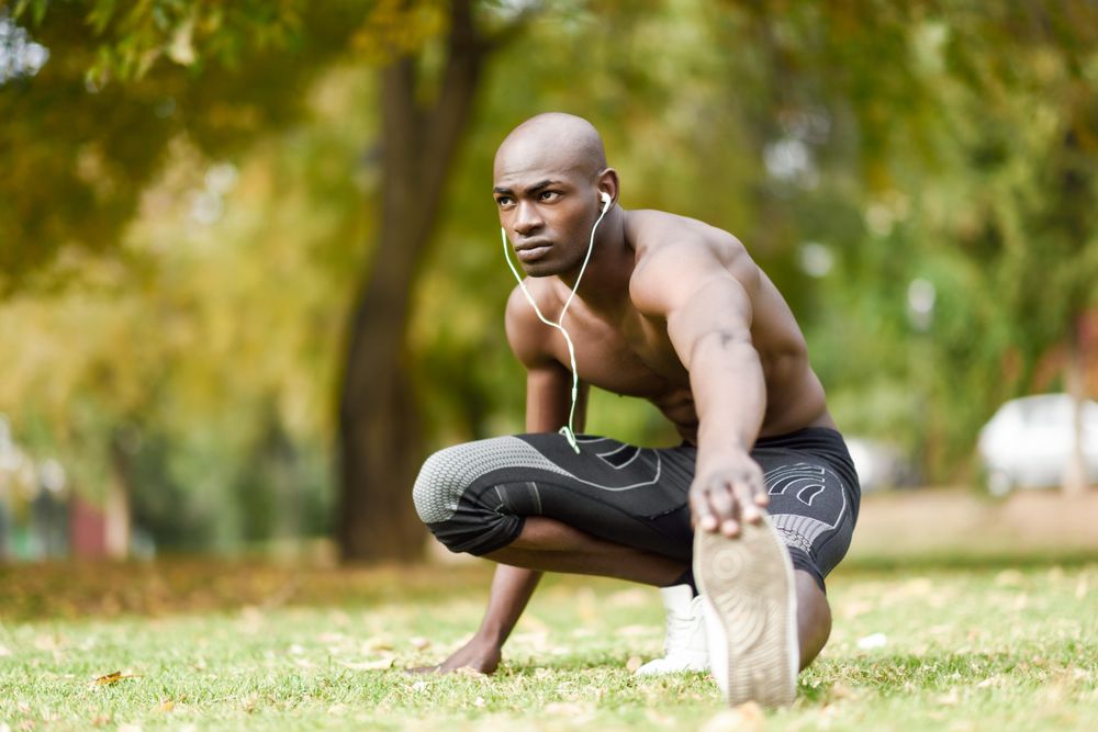 Fit male stretching lower body with shirt off listening to music on headphones