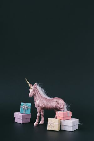 Pink glitter unicorn with wrapped presents on dark background