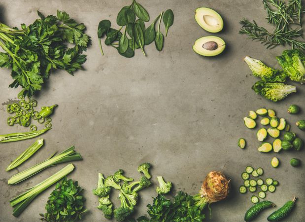 Arrangement of sliced green garden vegetables on concrete surface, copy space