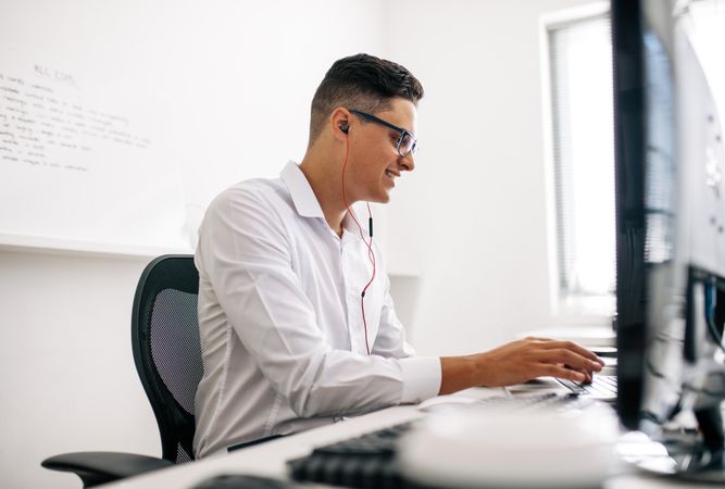 Man smiling and wearing spectacles working on laptop computer in office