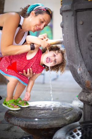Woman pouring water from fountain for child on street