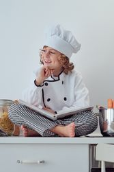 Happy preteen boy with cookbook sitting on kitchen cabinet