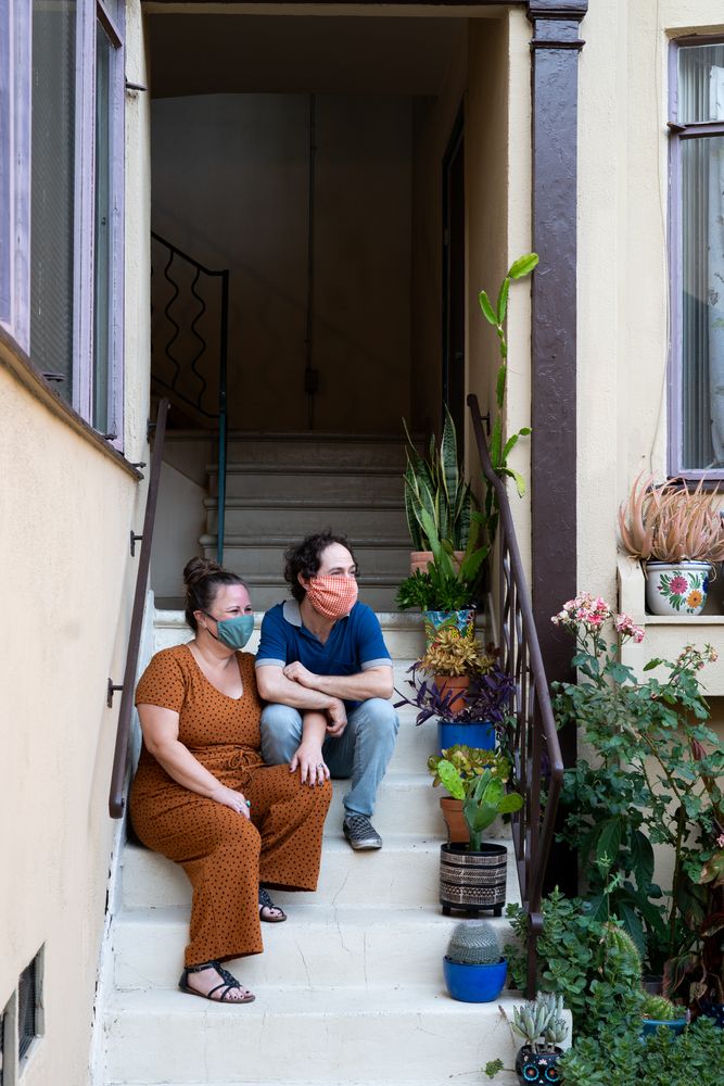 Loving couple sitting on stairs in front of apartment wearing masks and looking away