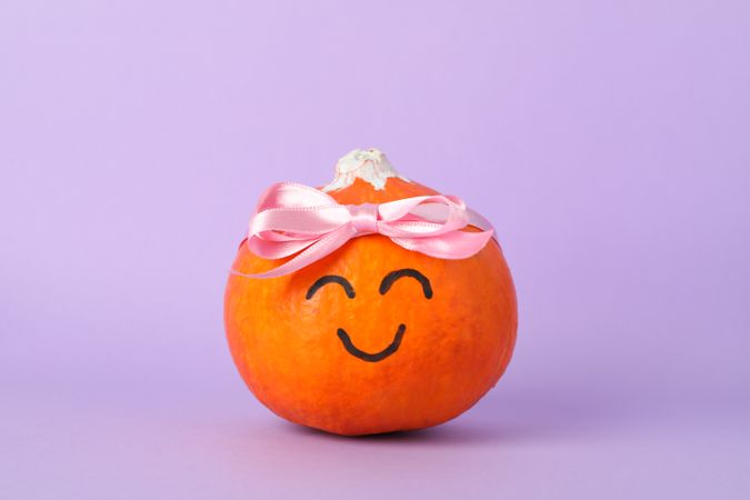 Pumpkin with smile and bow on violet background, space for text