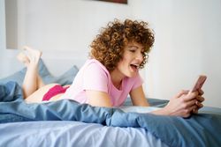 Surprised lying on her stomach in blue bed with her phone