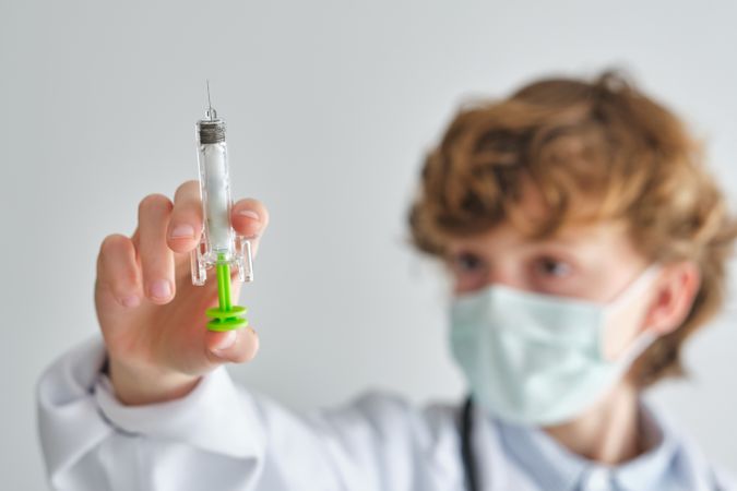 Attentive boy doctor in face mask with toy syringe