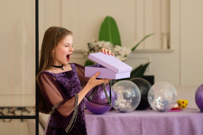 Girl excitedly opening gift box at birthday party.
