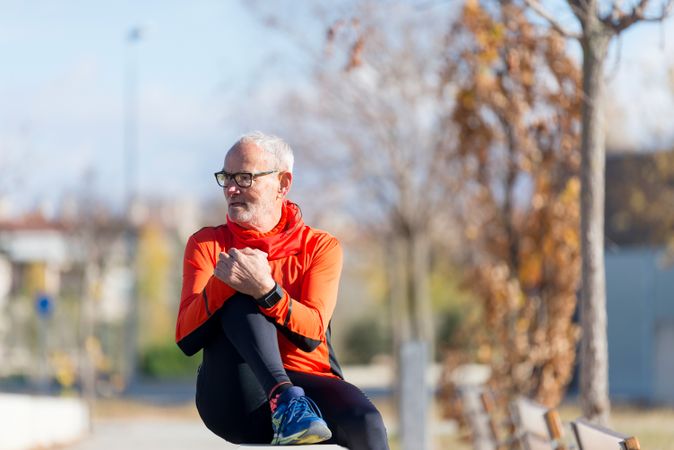 Older male holding knee while sitting on divide in park looking to his side