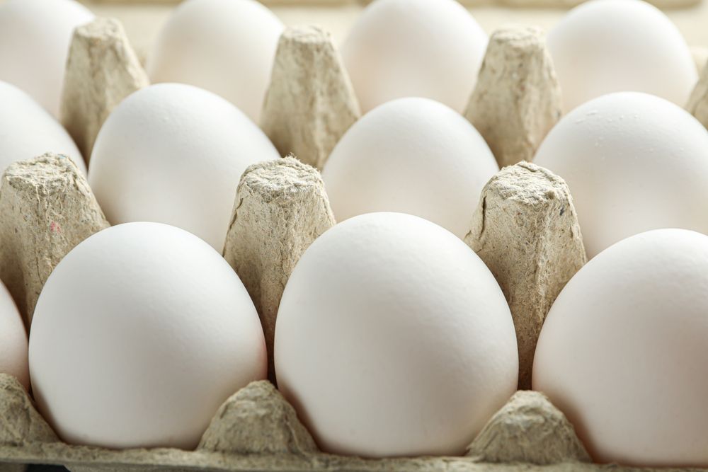 chicken eggs in carton box on wooden table, closeup
