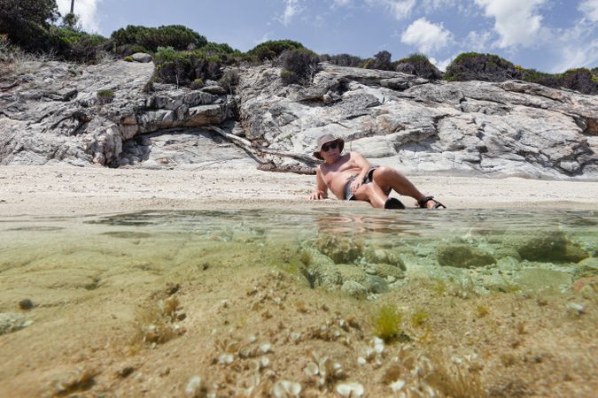 Man lying on sandy shore near water