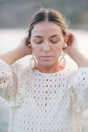 Feminine woman touching hair with closed eyes near sea