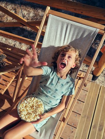 Cheerful boy with popcorn sitting in deckchair