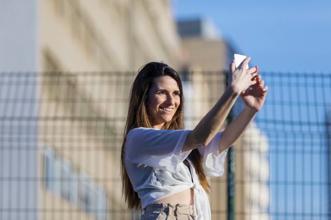 Smiling woman wearing casual wear standing in the street while taking a selfie on a sunny day