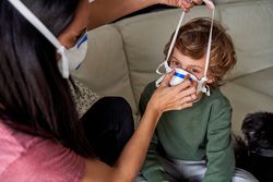 Female in protective mask putting respirator on son
