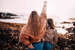 Two young women on the beach with one arm raised in victory