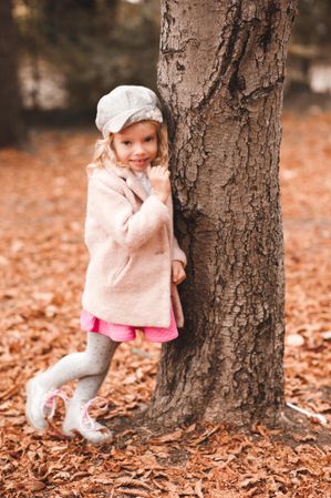 Young girl wearing pink jacket leaning on brown tree
