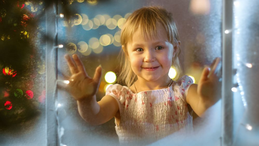 On Christmas Eve Cute Little Girl Looks Through the Window and Smiles.