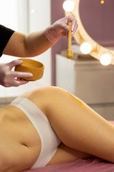 Warm honey is applied across client’s thigh during spa session.