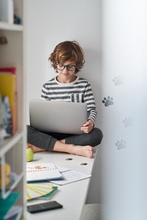 Boy using laptop while sitting on table in bedroom