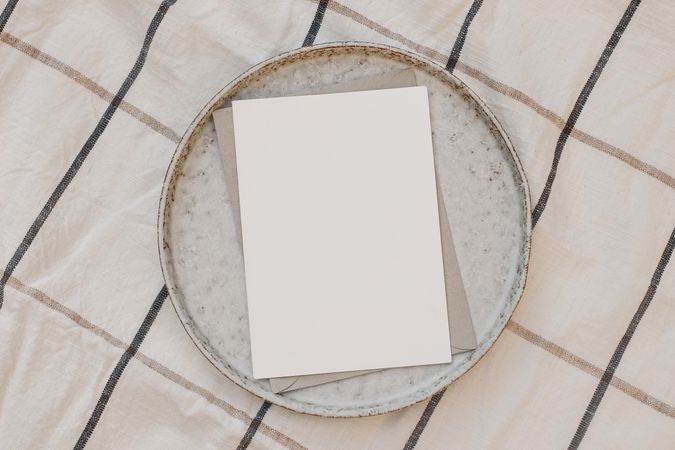 Blank greeting card with craft paper envelope on ceramic plate on striped dishtowel