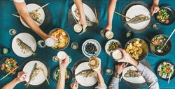 Flat-lay of human hands toasting with beer glasses over grilled sea bass, wide composition