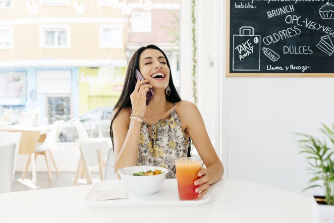 Cheerful woman with healthy food talking on smartphone in cafe