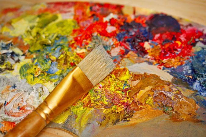 Paint brush lying on paint palette with rich colors