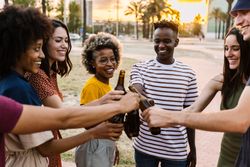 Multi-ethnic friends smiling and clinking their beer bottles together outside