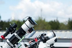 Telescopes on rooftop with cloudy sky background.