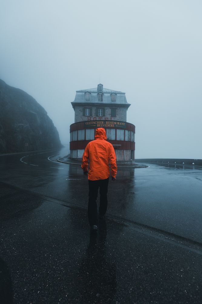Back view of person in orange jacket standing facing a store under rainy weather