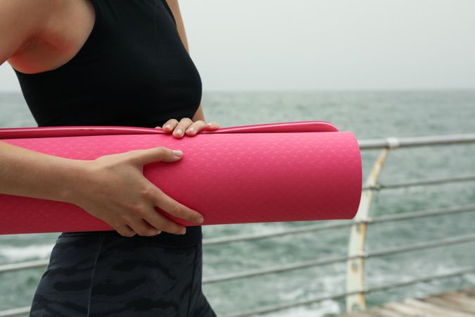 Pink yoga mat in female hands outdoors, close up