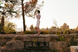 Woman in formal dress standing on stone house foundation with view of trees and sky