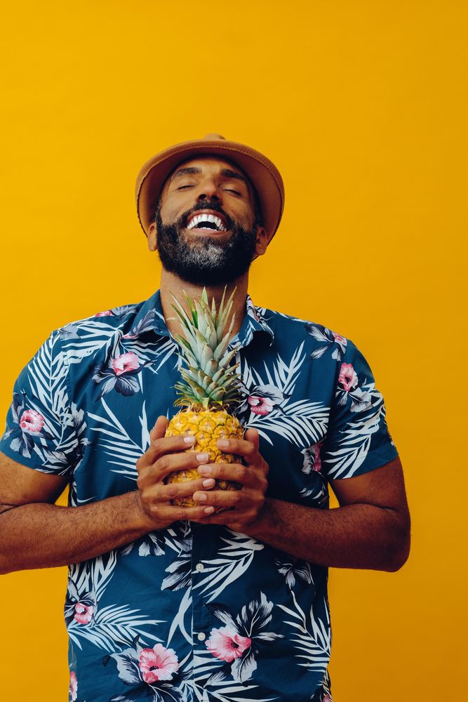 Calm male holding a pineapple to his chest in yellow studio