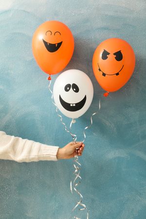 Female hand holding halloween balloons on color background