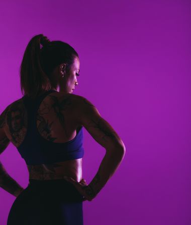 Rear shot of woman with tattoos looking down against a purple background
