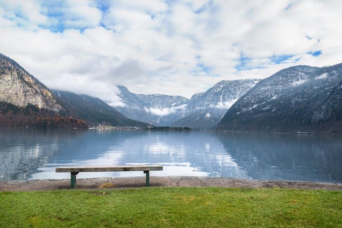 Wooden bench on calm alpine lakeshore with mountain views behind
