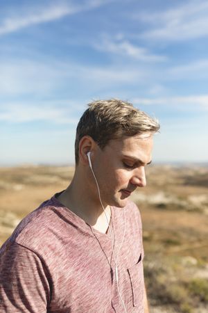 A man listens to music with headphones while thinking or meditating on a walk in the countryside and nature