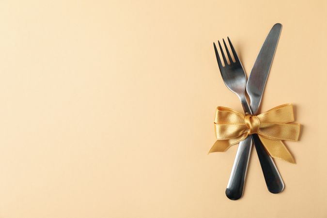 Cutlery with bow on beige background, space for text