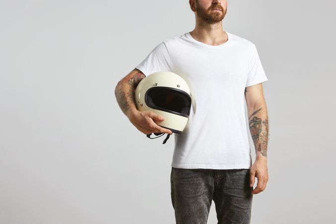 Tattooed man in light t-shirt holding motorcycle helmet