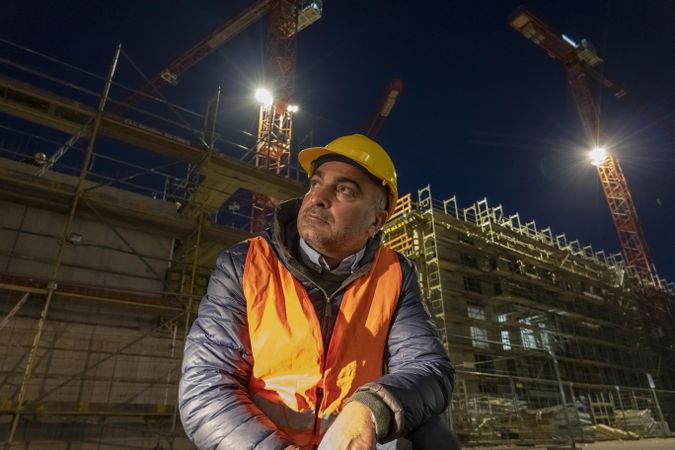 Construction worker sitting beside a building under construction at night